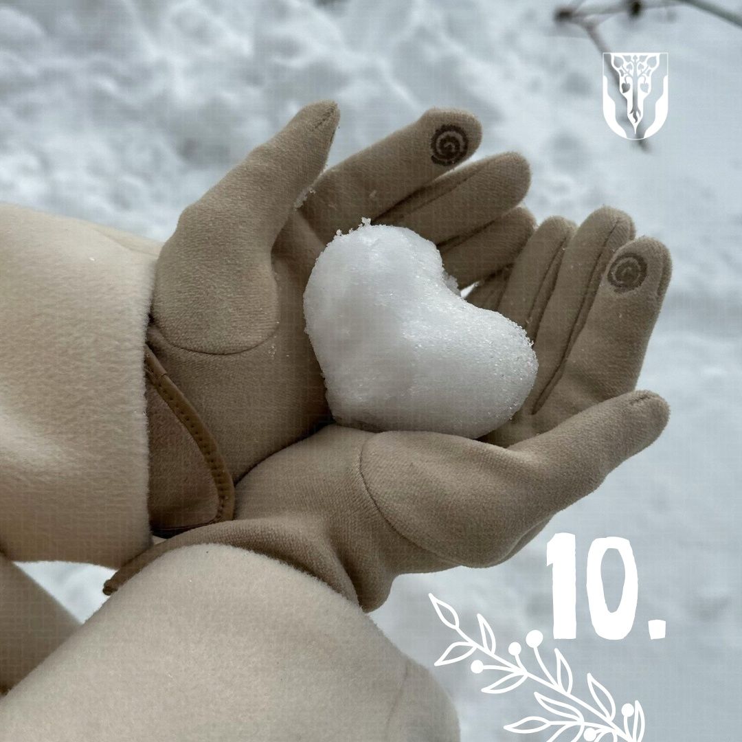 Eine Person in Handschuhen hält eine herzförmige Schneekugel. Sie befindet sich in einem verschneiten Bereich. Die Nummer 10 ist im Bild zu sehen.