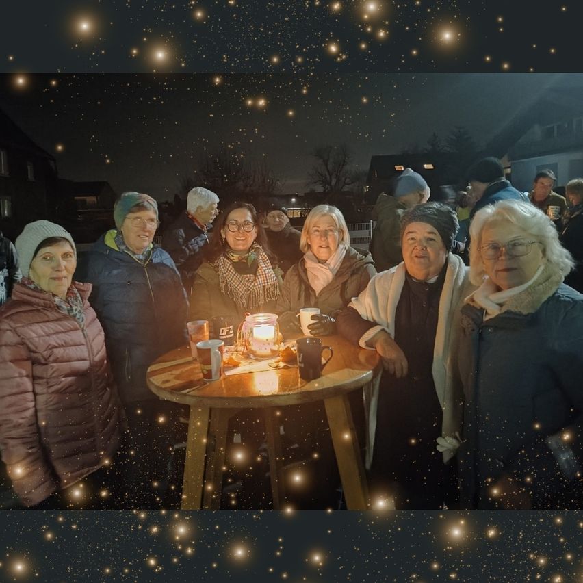 Eine Gruppe Erwachsener, einige mit Brille, stehen um einen Tisch mit brennenden Kerzen in Tassen, unter einem Sternenhimmel.
