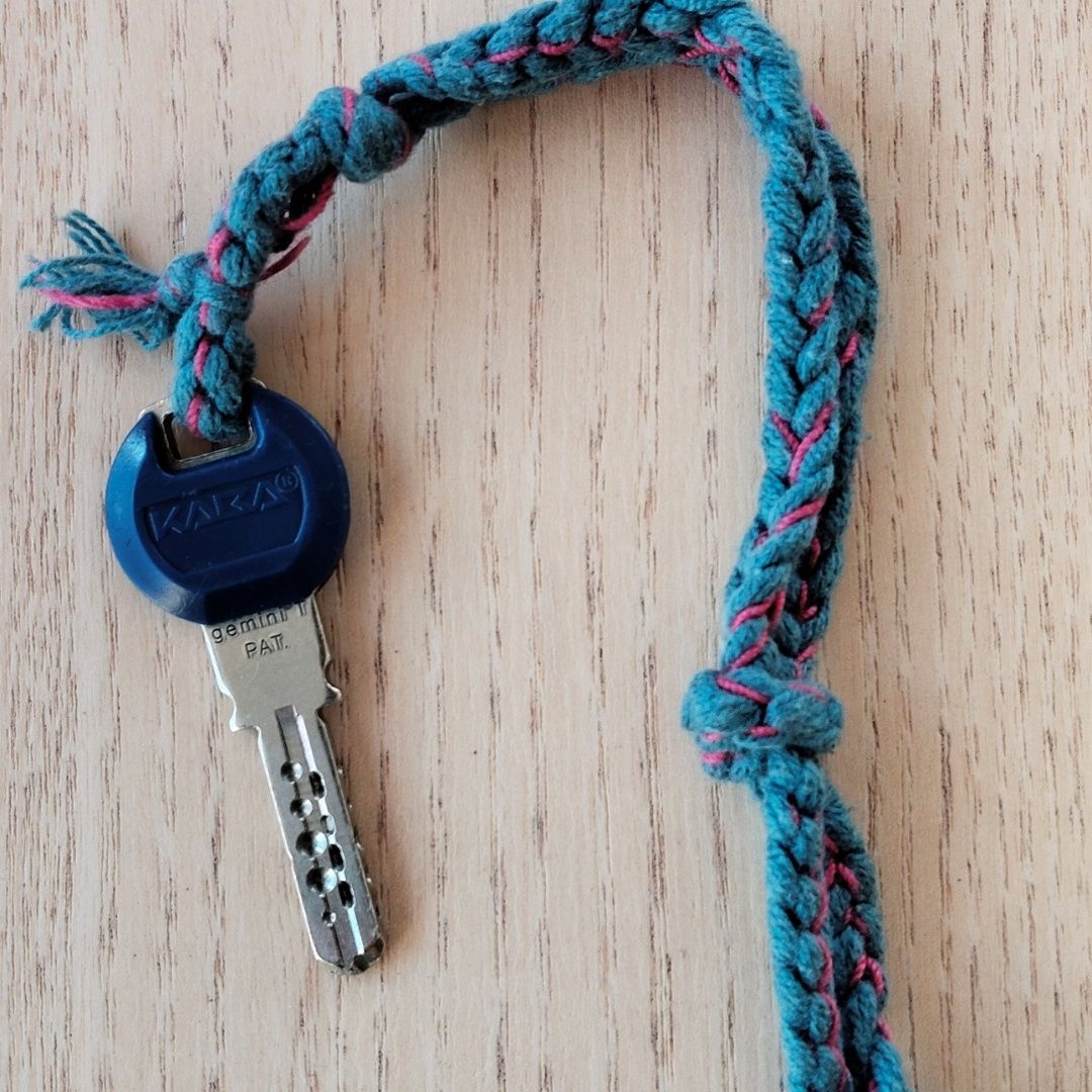 Ein blauer Schlüssel mit der Marke KAXA und Gemini PAIT ist an einer geflochtenen blauen und rosa Schnur auf einer Holzoberfläche befestigt.