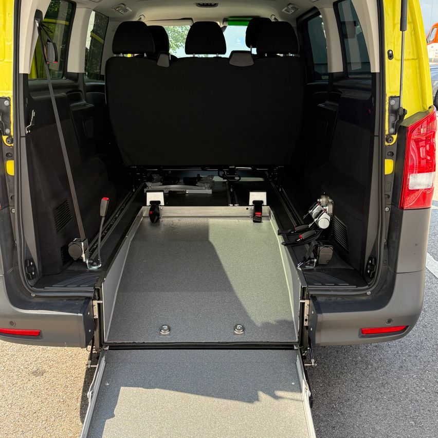 The back of a yellow and gray van with its rear door open, showing the interior with a wheelchair ramp and seating.