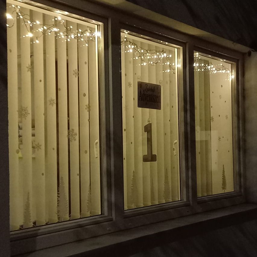 Ein Fenster zeigt dekorative Lichter und Schneeflocken. Ein Schild auf dem Fenster steht Adventszeit. Die Nummer 1 ist auf dem Fenster angezeigt.