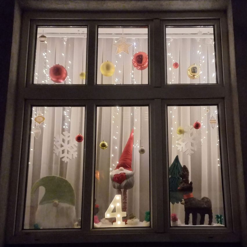 Ein Fensterdisplay mit Weihnachtsdekorationen, darunter Ornamente, Schneeflocken und eine Figur des Weihnachtsmanns mit der Nummer 4. Es gibt auch Rentiere und Weihnachtsbäume.