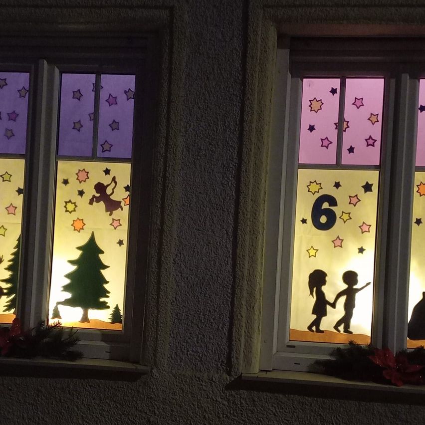 Two windows with festive decorations. The left window features a Christmas tree and angel. The right window shows two children holding hands with the number 6 above.