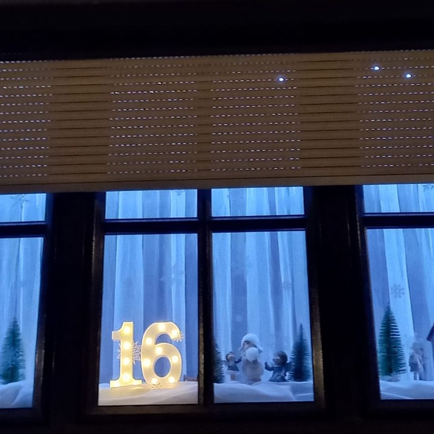 Ein Fenster zeigt die leuchtende Nummer 16 mit einer verschneiten Szene dahinter, mit Weihnachtsfiguren, Bäumen und Schneeflocken.