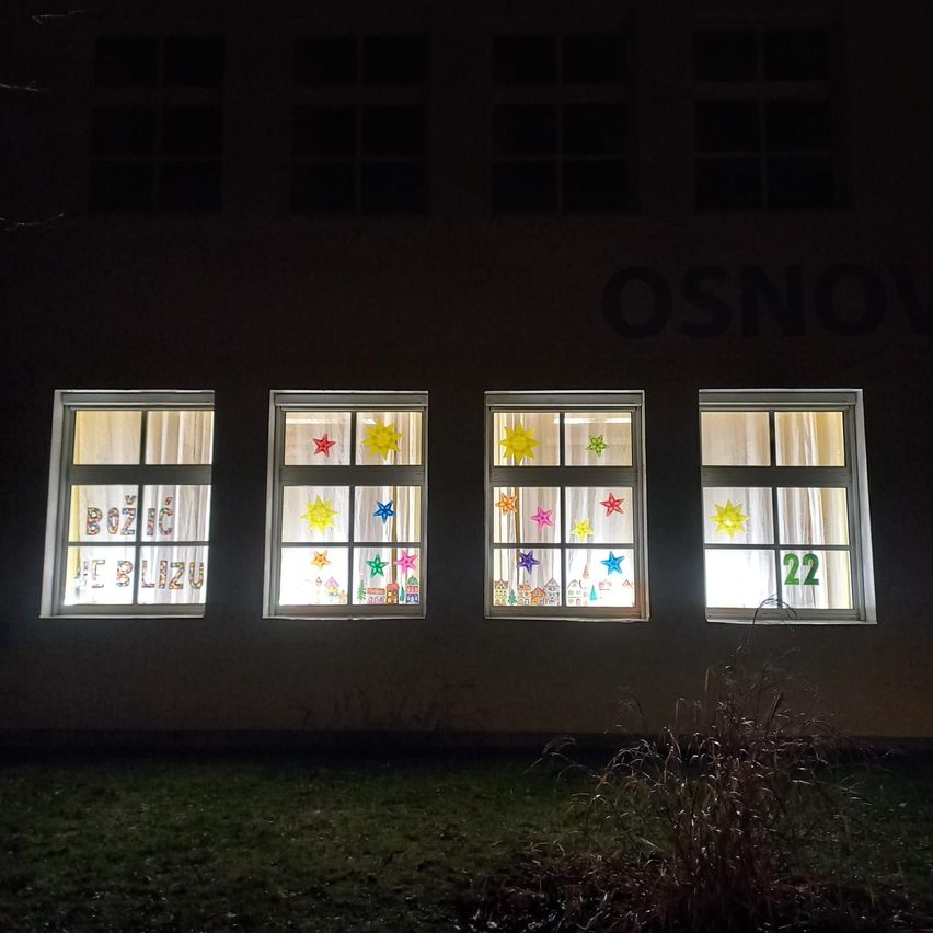 Vier Fenster eines Gebäudes bei Nacht, jedes zeigt eine festliche Szene mit Sternen und Zahlen. Das erste Fenster hat '2020', das zweite '2021', das dritte eine sternenbesetzte Szene und das vierte '22'.