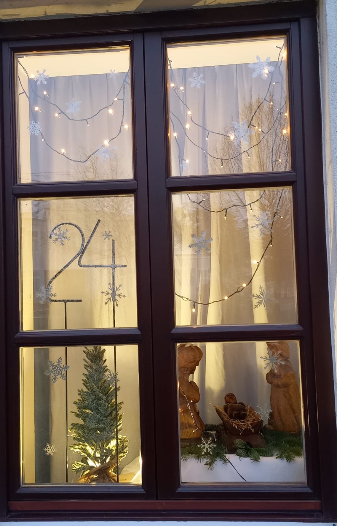 Ein weihnachtliches Fensterdisplay mit einem kleinen Weihnachtsbaum und Schneeflocken. Die Nummer 24 ist auf das Fenster gemalt.