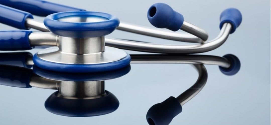 Eine Nahaufnahme eines blauen und silbernen Stethoskops auf einer reflektierenden Oberfläche. Das Stethoskop ist glänzend, und die Ohrstücke sind schräg.