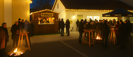 Eine nächtliche Szene mit Menschen, die sich um ein Feuerbecken versammelt haben. Ein Stand mit einem Schild, das 'Punsch' liest, ist in der Nähe. Der Bereich ist gut beleuchtet mit Lichterketten.