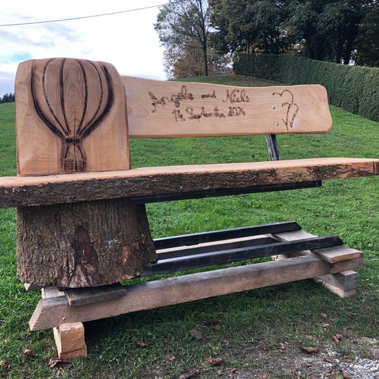Eine Holzbank mit einer Inschrift auf der Rückenlehne steht auf einem Rasen.