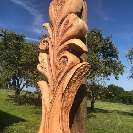 Eine große Holzschnitzerei einer Blume steht an einem sonnigen Tag auf einer Wiese.