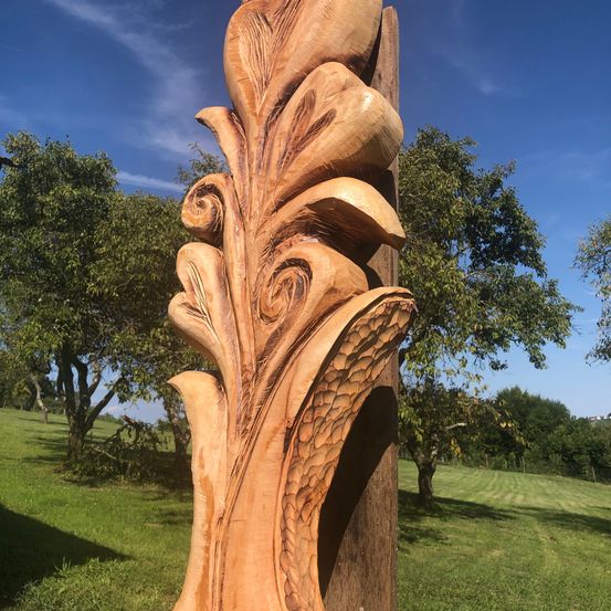 Eine große Holzschnitzerei einer Blume steht an einem sonnigen Tag auf einer Wiese.