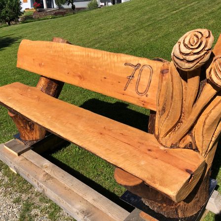 Eine Holzbank mit der Nummer 70 und drei geschnitzten Blumen in einer Grasfläche