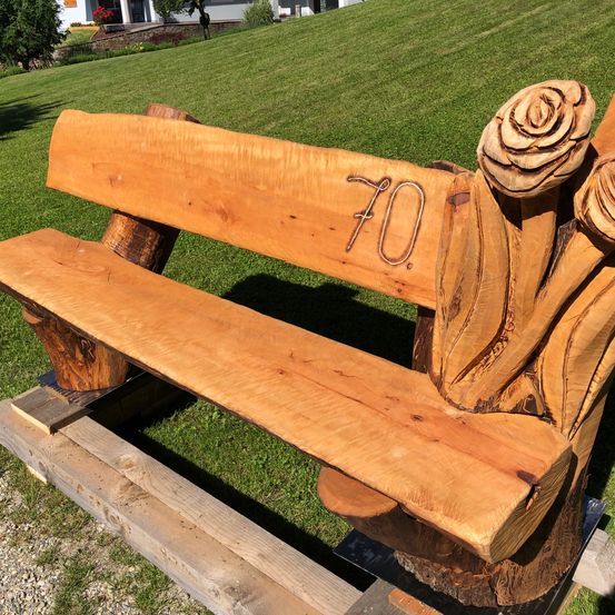 Eine Holzbank mit der Nummer 70 und drei geschnitzten Blumen in einer Grasfläche