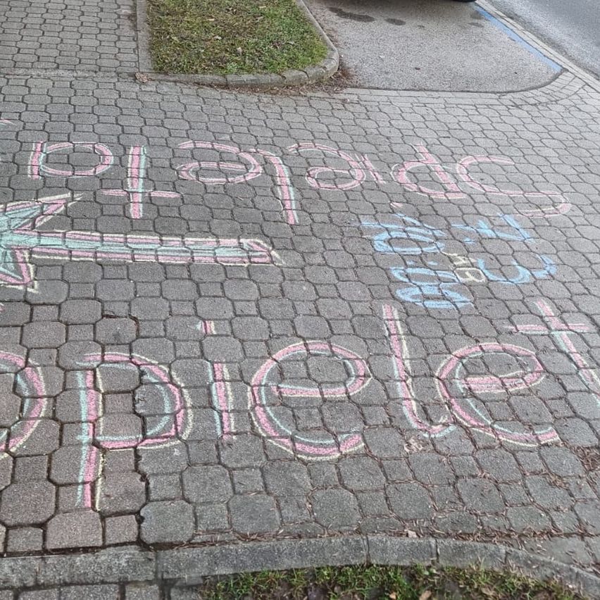 Ein Kreidezeichnung auf einem Bürgersteig zeigt 'Doppelt' mit einem Pfeil nach rechts. Darunter steht ein kleineres Wort 'doppelt' und einige zusätzliche Schriftzüge.