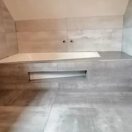 Ein modernes Badezimmer mit grauen Fliesen und einer Badewanne an einer gefliesten Wand. Es gibt zwei Metallbeschläge an der Wand.