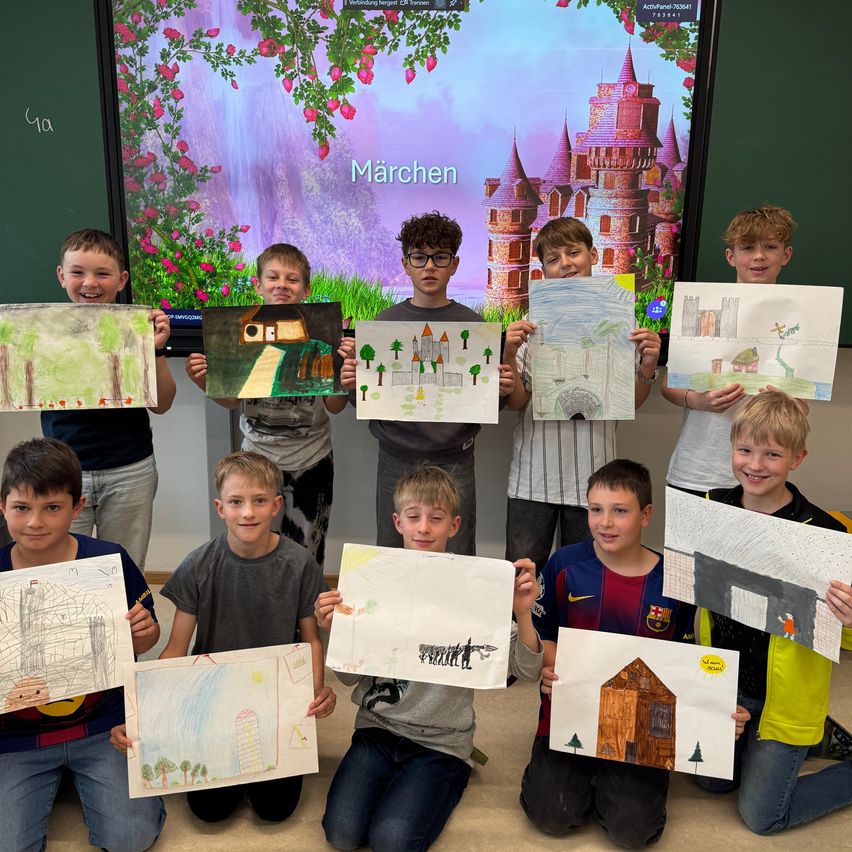 Eine Gruppe von Jungen sitzt auf dem Boden und hält Zeichnungen hoch, lächelt. Hinter ihnen zeigt eine Leinwand eine Burg und Blumen. Das Wort Märchen ist auf dem Bildschirm zu sehen.
