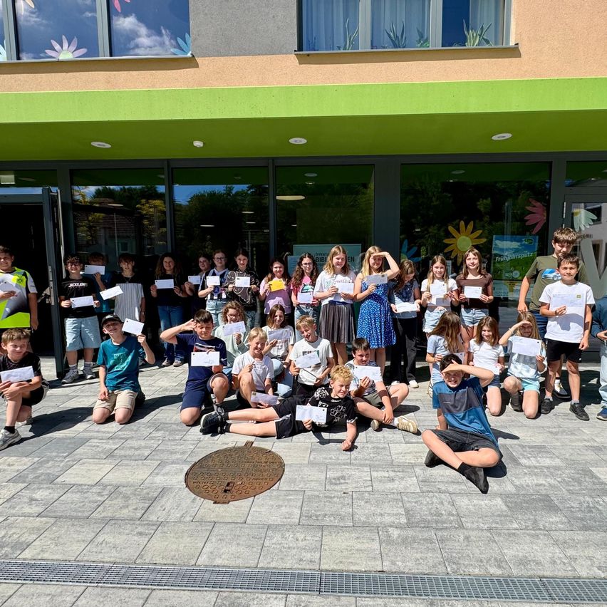 Eine Gruppe von Kindern und Erwachsenen posiert für ein Foto vor einem Gebäude. Sie halten Zertifikate und sehen fröhlich aus.