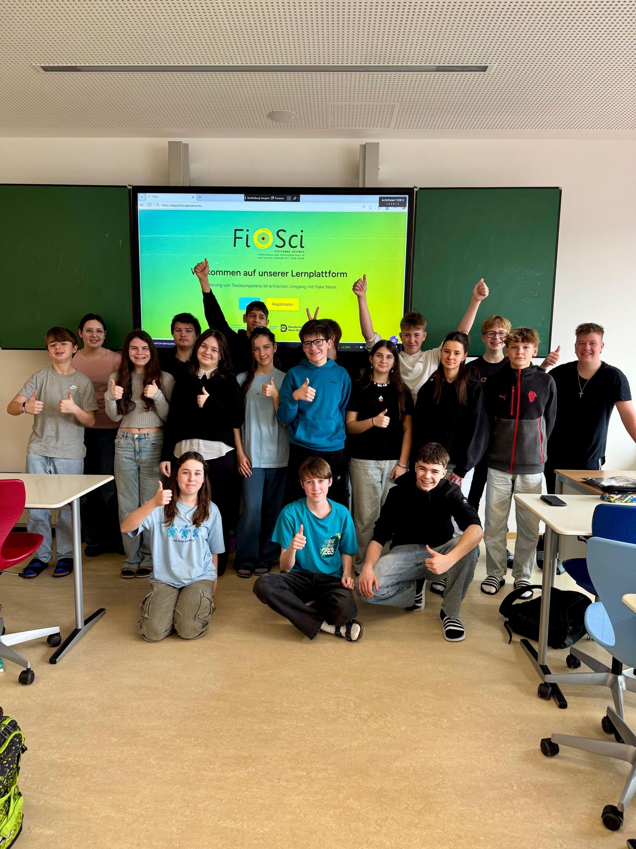Eine Gruppe von Schülern posiert für ein Foto in einem Klassenzimmer mit einer Projektionsleinwand, die die Fi o Sci Lernplattform zeigt.