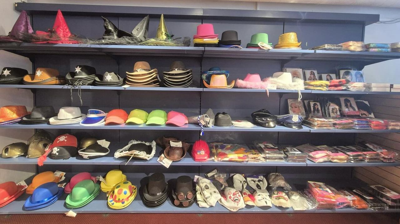 A shelf with multiple hats and masks displayed. Hats include cowboy, conical, and various colors. Masks range from horror to clown themes.