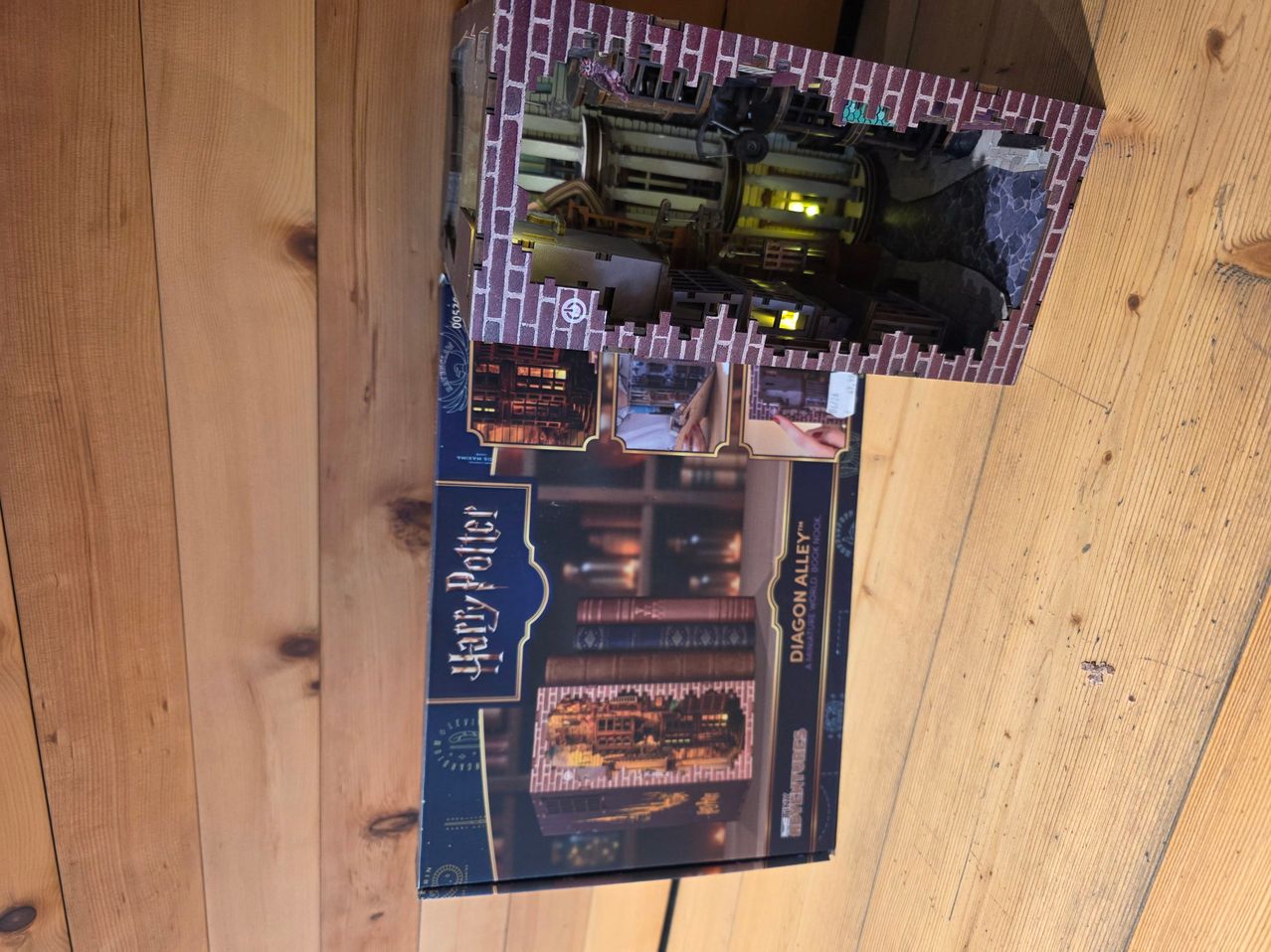 A box of a Harry Potter Diagon Alley model kit, opened to reveal the interior design. The box is placed on a wooden surface.