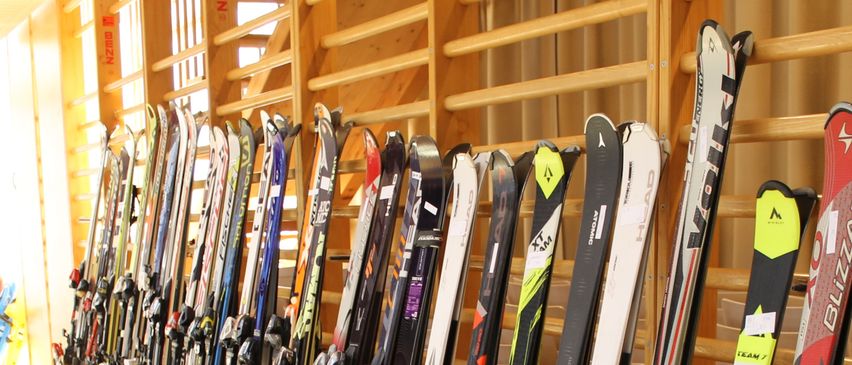 Ein Skiladen zeigt eine Reihe verschiedener Skier, die an einer Holzwand montiert sind und verschiedene Farben und Marken präsentieren.