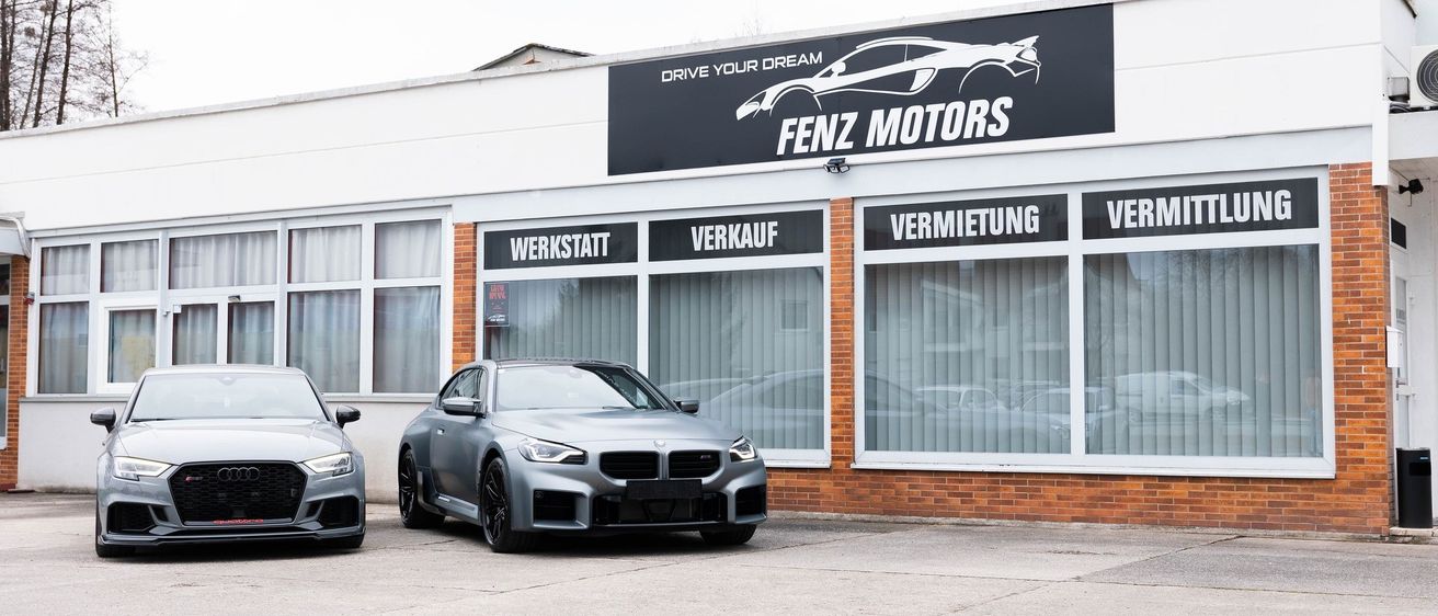 Zwei Autos stehen vor einem Gebäude mit 'FENZ MOTORS' über dem Eingang. Das Gebäude bietet Dienstleistungen wie Werkstatt, Verkauf, Vermietung und Verleih an.