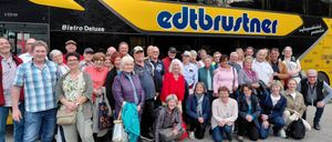 Eine Gruppe von Menschen posiert vor einem edtbustn-Bus, mit Bäumen und klarem Himmel im Hintergrund.