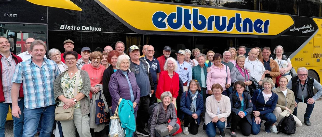 Eine Gruppe von Menschen posiert vor einem edtbustn-Bus, mit Bäumen und klarem Himmel im Hintergrund.