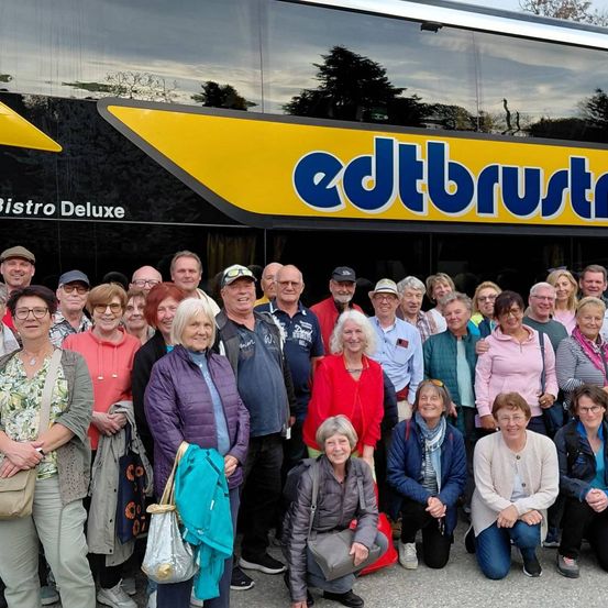 Eine Gruppe von Menschen steht vor einem Bus mit den Worten edtbrustle Bistro Deluxe darauf. Sie alle lächeln und scheinen auf einer Reise zu sein.