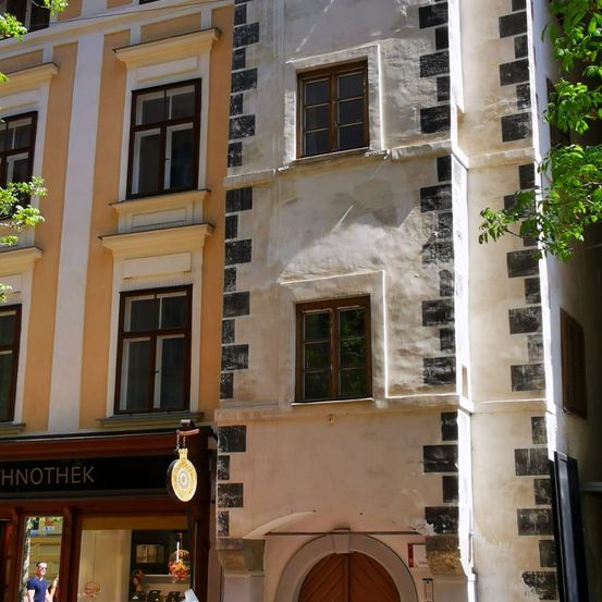 Ein Gebäude mit einer Holztür und mehreren Fenstern. Ein Schild unter dem Fenster steht 'CHNOTHEK'. Ein Mann in Blau ist im Schaufenster.