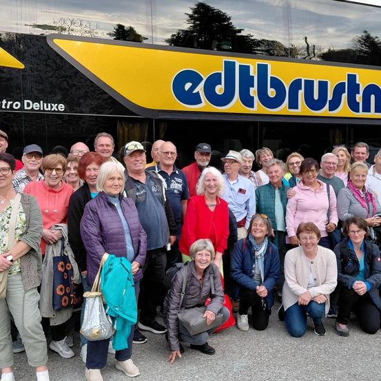 Eine Gruppe von Menschen posiert für ein Foto vor einem edtbustn-Bus. Der Bus hat ein gelbes und blaues Schild. Sie alle lächeln.