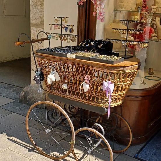 Ein dekorativer Weidenkorbwagen mit Schmuckablagen und Accessoires vor einem Laden ausgestellt.
