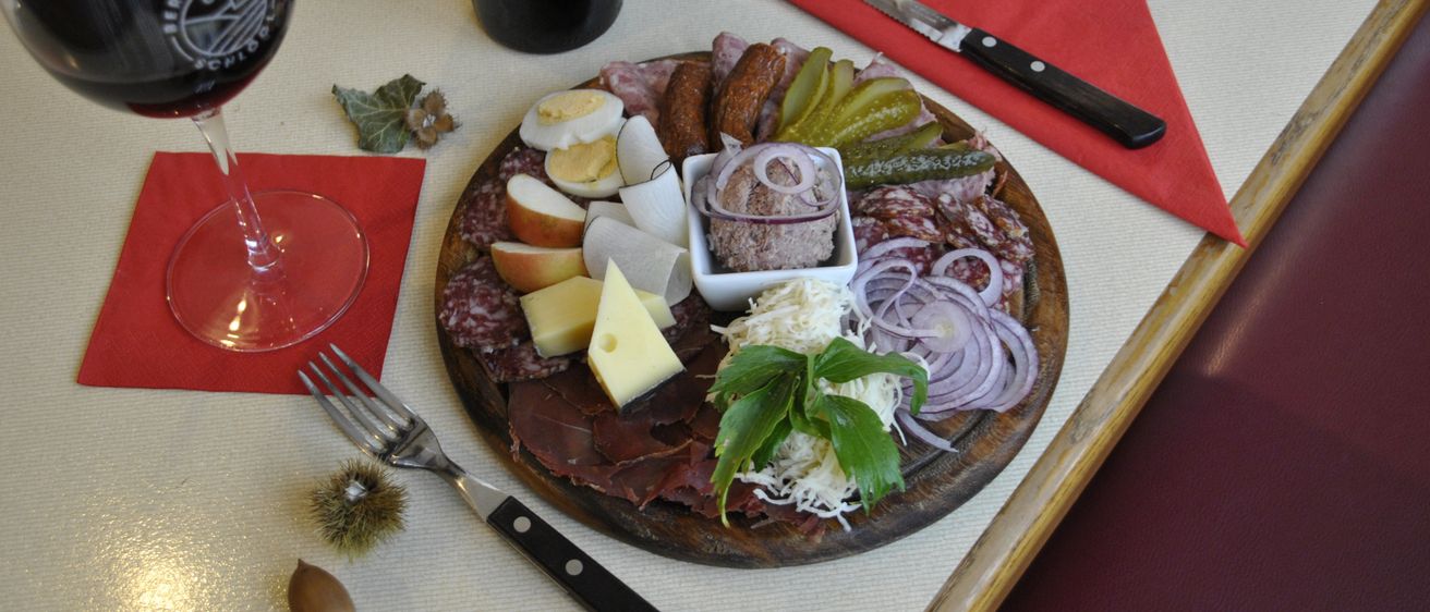 Eine Charcuterie-Platte mit verschiedenen Fleischsorten, Käse, Gurken und einer Flasche Wein steht auf einem Tisch.