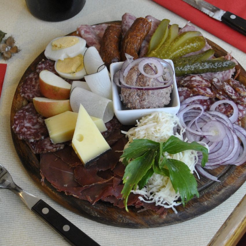 Eine Charcuterie-Platte mit verschiedenen Fleischsorten, Käse, Gurken und einer Flasche Wein steht auf einem Tisch.