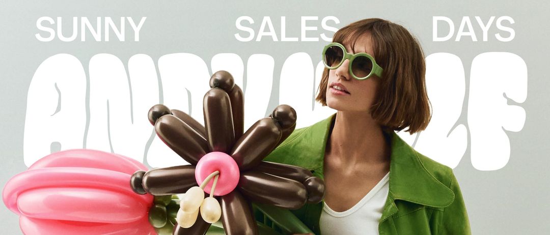 Eine Frau in einer grünen Jacke und karierter Schürze hält eine bunte Ballonblume und steht vor grauem Hintergrund. Veranstaltungsdetails: 9. April, 10-20 Uhr und 10. April, 10-17 Uhr, Andy Wolf, Hartberg-Filiale.