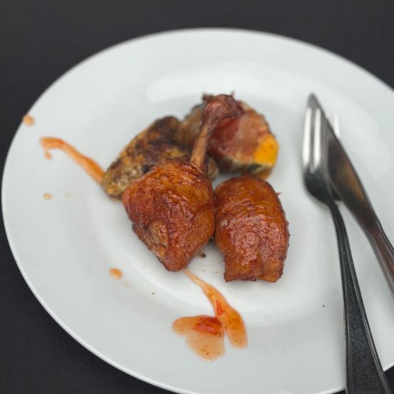 Ein weißer Teller enthält gebratene Fleischstücke, mit roter Soße und Besteck in der Nähe. Das Fleisch ist glasiert und zeigt Anzeichen, frisch serviert worden zu sein.