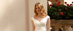 Eine Frau in einem weißen Hochzeitskleid steht auf einer Steintreppe mit einer Brüstung im Hintergrund.