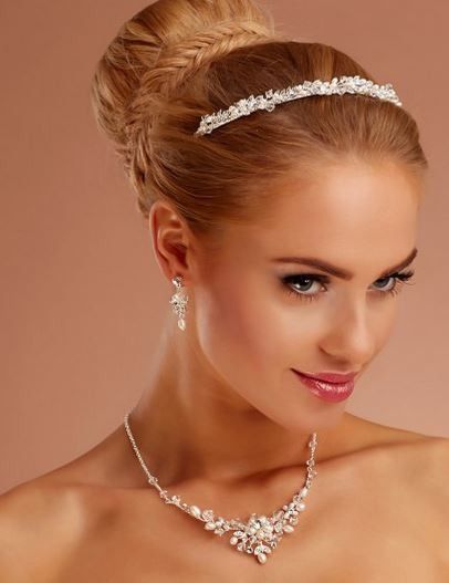 Eine Frau mit blondem Haar trägt eine funkelnde Tiara, Ohrringe und eine Halskette. Sie schaut direkt in die Kamera und trägt Make-up.