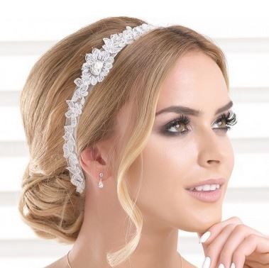 Eine blonde Frau mit Make-up und einer Spitzenkopfband posiert für ein Foto. Sie trägt eine Halskette und Ohrringe.