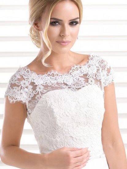 Eine Braut mit blonden Haaren, die ein weißes Hochzeitskleid mit Spitze trägt, posiert für ein Foto.