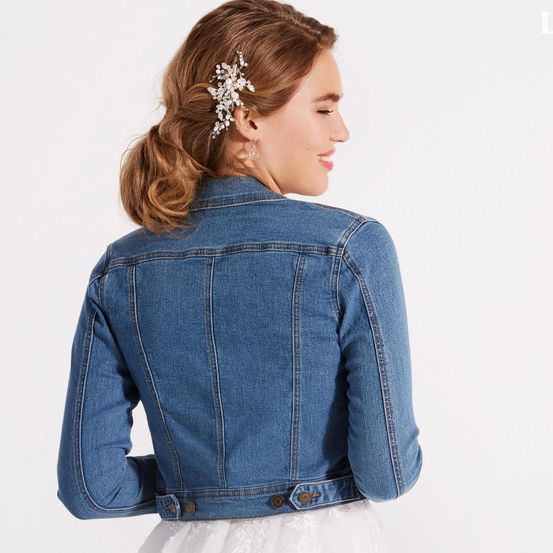 Eine Frau, die eine Jeansjacke mit einer Blumenhaarnadel und Ohrringen trägt, von hinten gesehen.