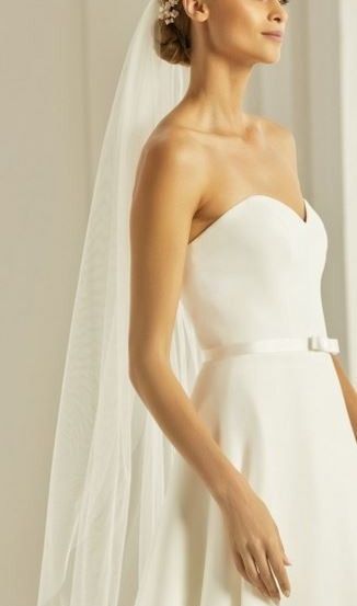 Eine Frau in einem weißen Hochzeitskleid mit Schleier und Blumenkranz posiert für ein Foto.