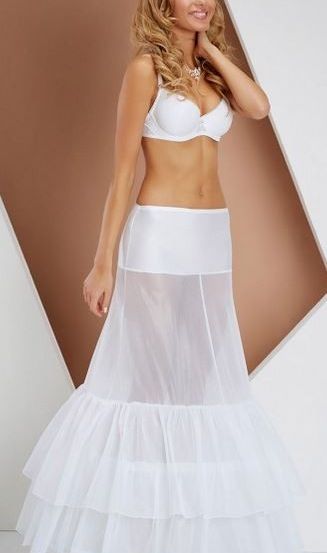 Eine Frau in einem weißen Bikini und einem weißen, mehrschichtigen Rock posiert für ein Foto.