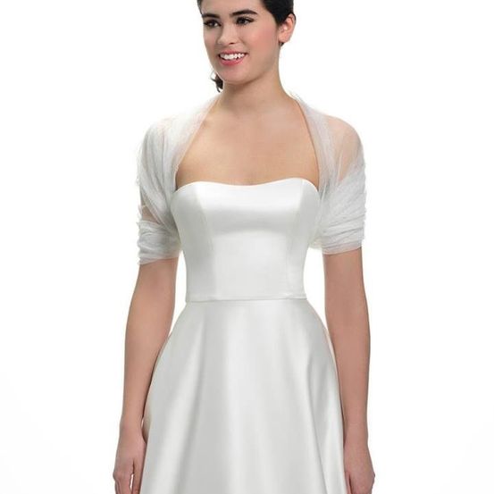Eine Frau in einem weißen Hochzeitskleid posiert für ein Foto mit einem durchsichtigen Umhang über den Schultern.