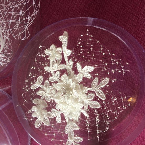 Ein Spitzendesign auf einem durchsichtigen Kunststoffkreis, das einer Blume mit komplizierten Details und schleierartiger Textur ähnelt, auf einer braunroten Oberfläche platziert.