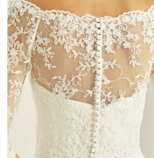 Ein weißes Hochzeitskleid mit off-shoulder Spitzenärmeln und einem Blumen-Spitzenmuster. Der Miederteil hat Perlknöpfe und ein netzartiges Material.