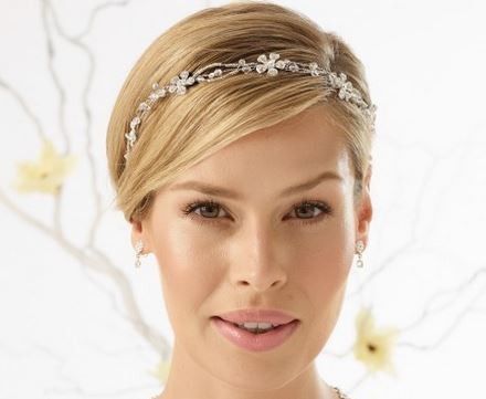 Eine Frau mit blondem Haar trägt eine Diamantkopfbedeckung und Ohrringe und posiert lächelnd für ein Foto.