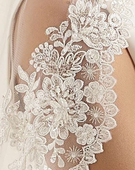 Eine Nahaufnahme von weißem Spitzenstoff mit Blumenmustern, möglicherweise Teil eines Hochzeitskleides.