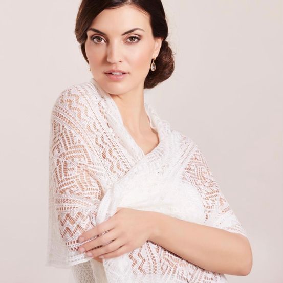 Eine Frau posiert für ein Foto, trägt einen weißen Spitzenschal um die Schultern und lächelt leicht.