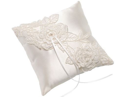 Ein weißer Kissen mit aufwendigen Spitzendesigns, einschließlich Blumen und Blättern, wird auf weißem Hintergrund gezeigt. Es hat einen Perlenknopf und eine weiße Schleife.